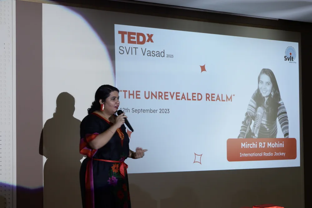 A speaker presenting beside their title slide and photo