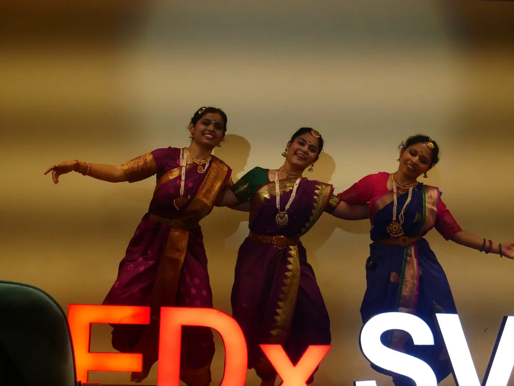 Three dancers performing beside the illuminated TEDxSVIT sign